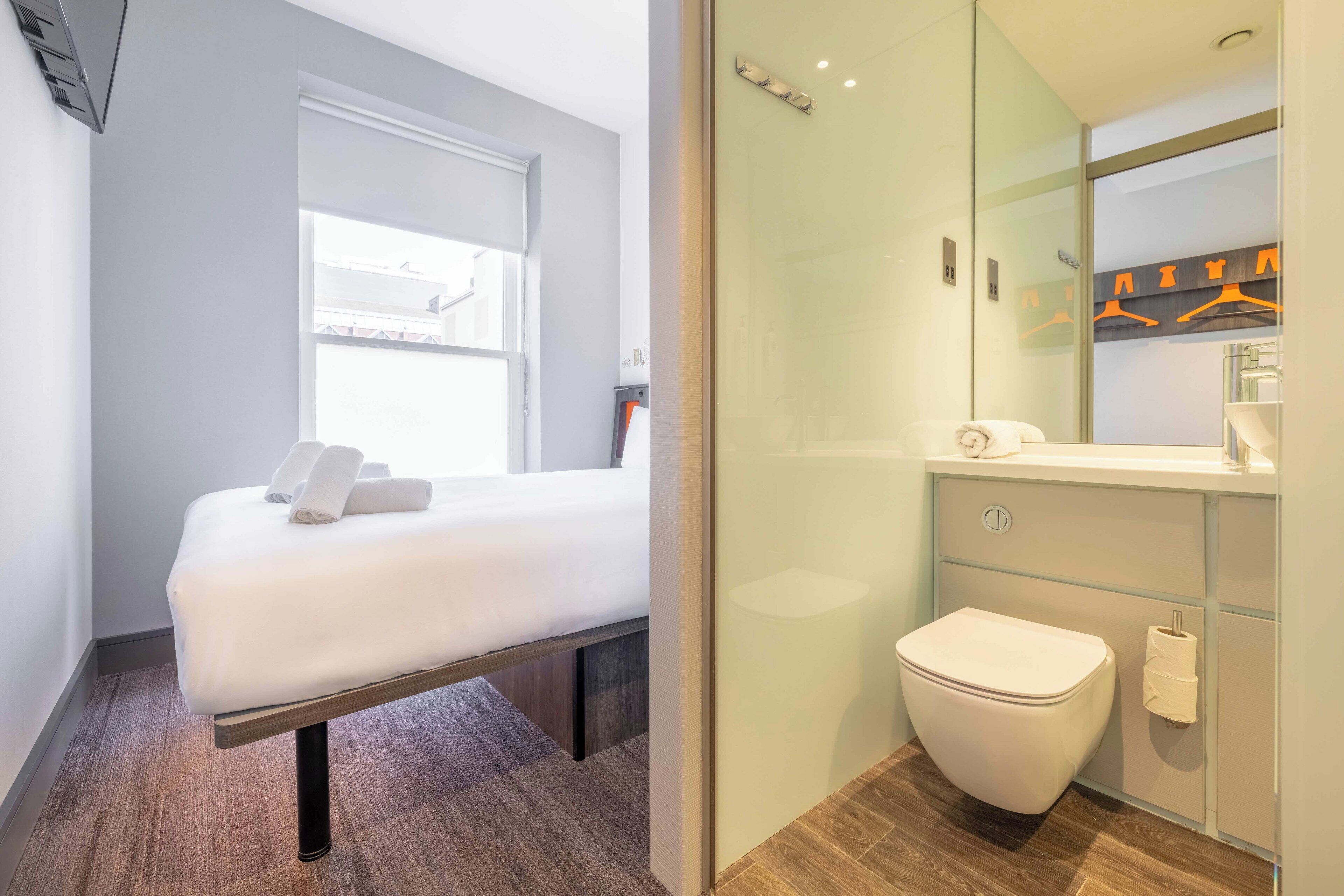 Una camera d'albergo moderna con un letto, un bagno con il water e uno specchio.