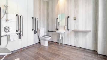 Un baño moderno con inodoro, bidé y lavamanos, equipado con barras de apoyo y un espejo.