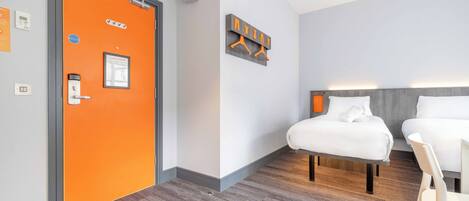 Une chambre d’hôtel avec une porte d’un orange vif, un lit avec une literie blanche, une tête de lit en bois et un luminaire fixé au mur.