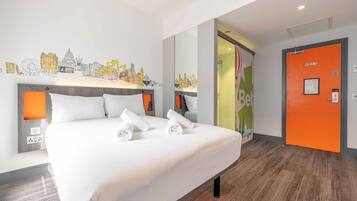 A hotel room with a large bed, two bedside tables with lamps, a cityscape mural on the wall, and an orange door.