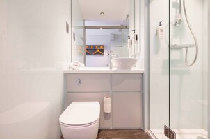 Un baño moderno con cabina de ducha de vidrio, un lavabo blanco y un inodoro.