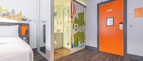 Una habitación de hotel con cama, un baño con cabina de ducha de vidrio y una puerta naranja.