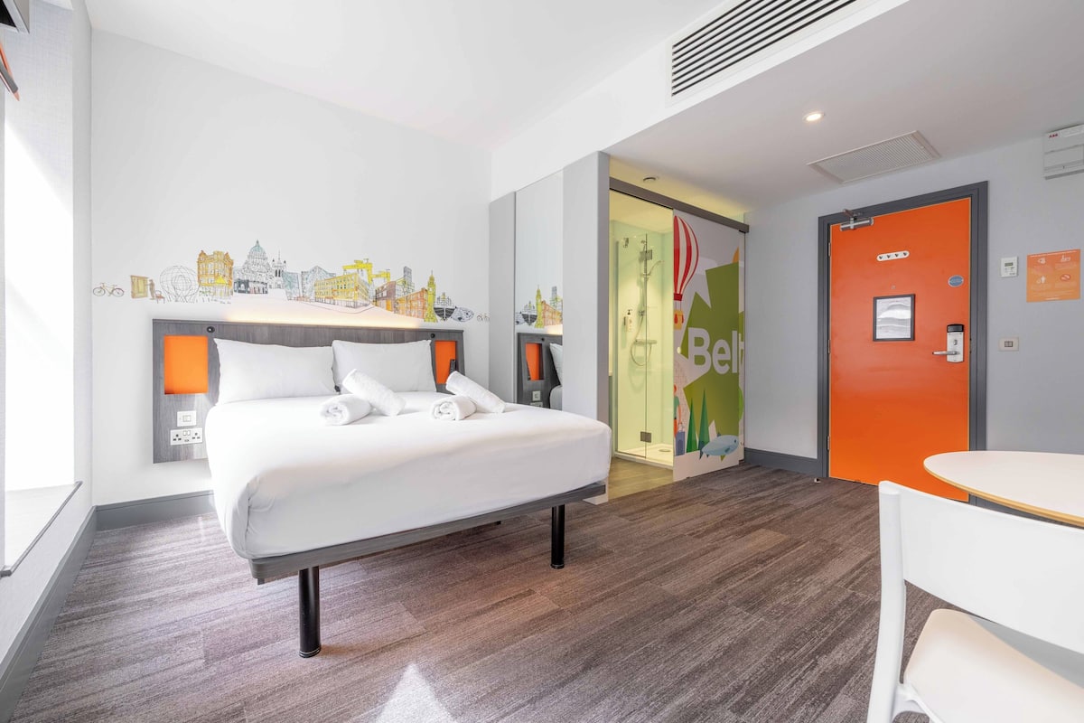 A hotel room with a bed, a desk, and a bathroom visible through an open door.