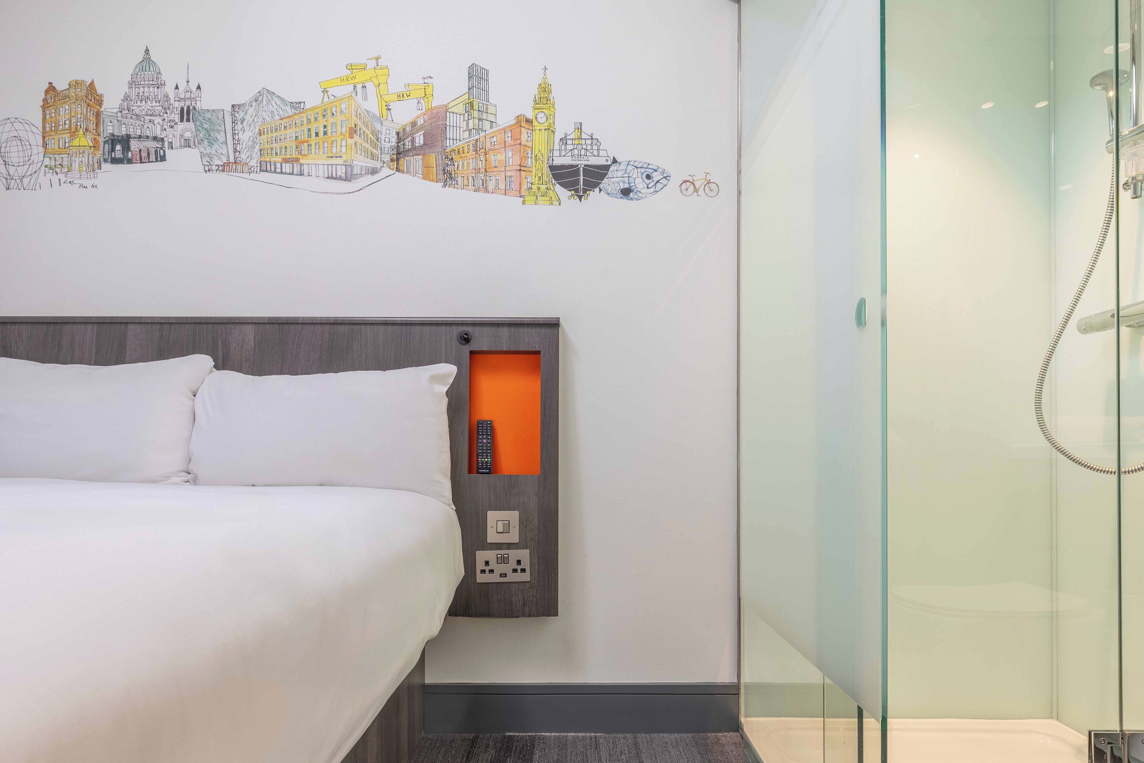 Une chambre d’hôtel équipée d’un lit, d’un panneau de commande fixé au mur et d’une cabine de douche en verre.