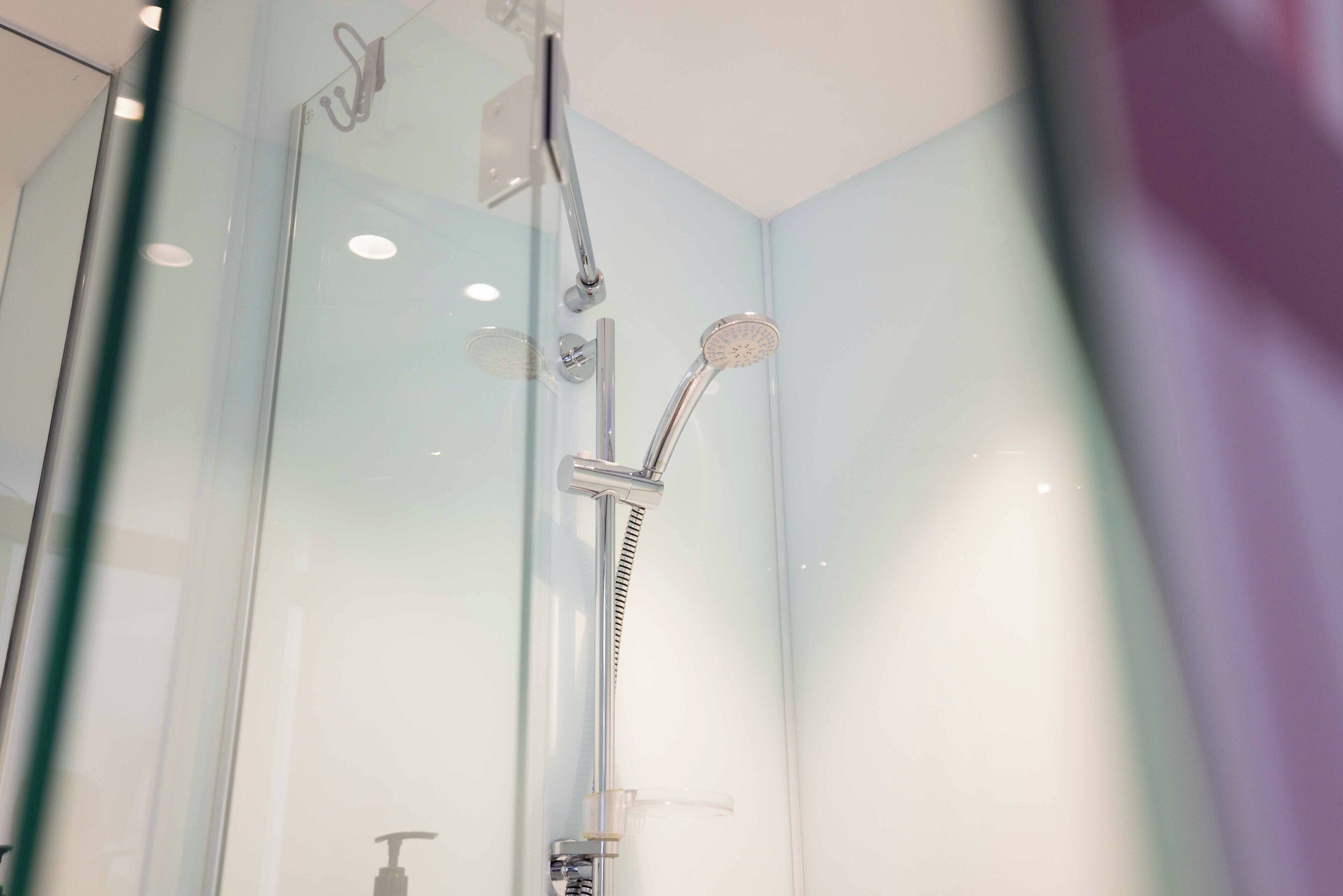 A glass-enclosed shower with a handheld showerhead and a wall-mounted faucet.