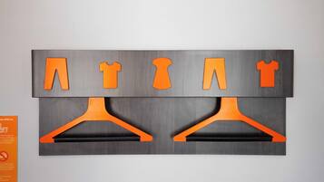 Un mur orné d’un panneau gris sur lequel sont découpées des formes orange représentant un cintre, une chemise et un pantalon.