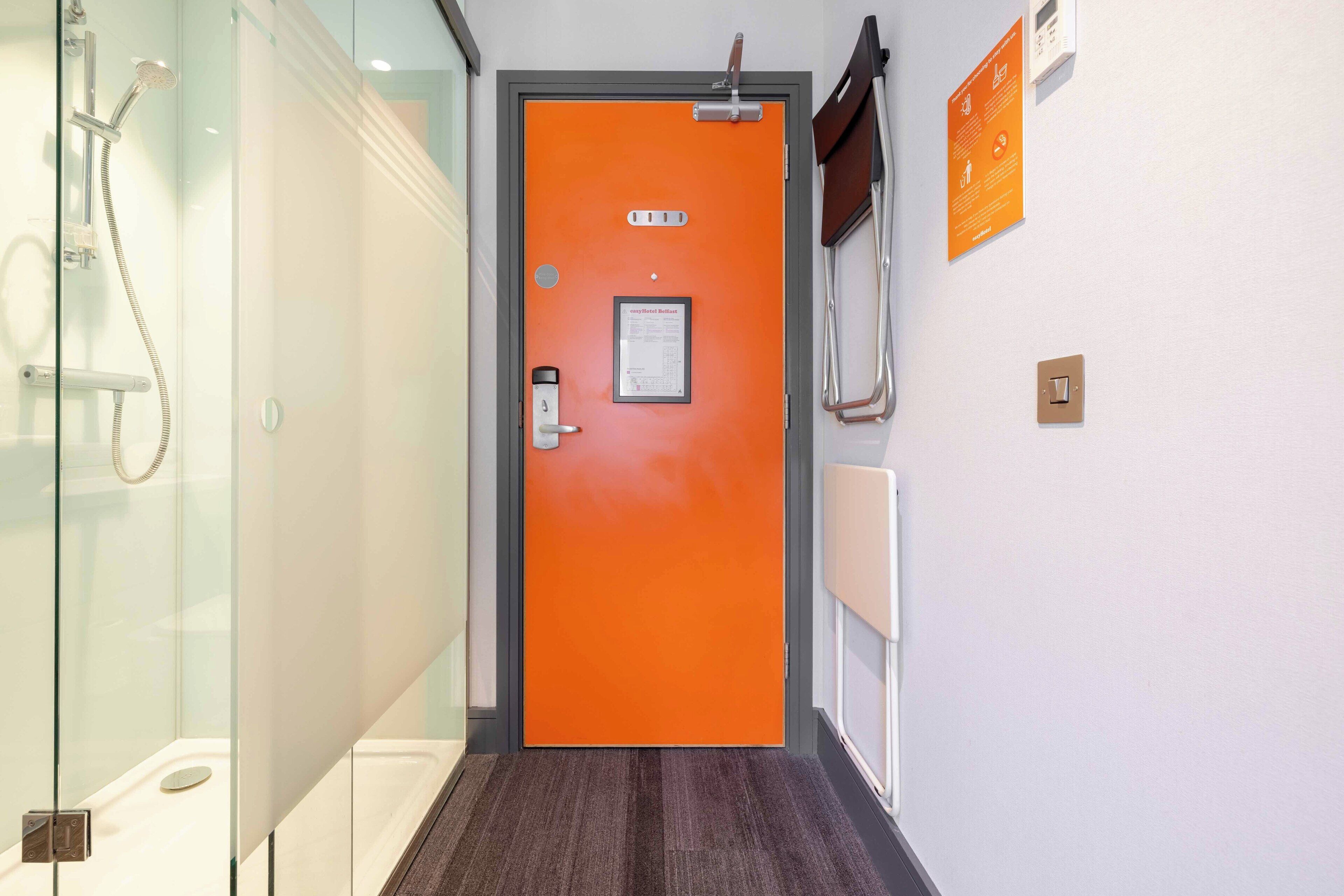 A hallway with an orange door, a glass shower enclosure, and a sign on the wall.
