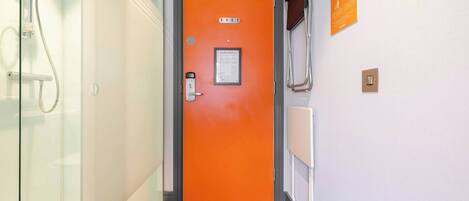 Un pasillo con una puerta naranja, un box de ducha de vidrio y un letrero en la pared.