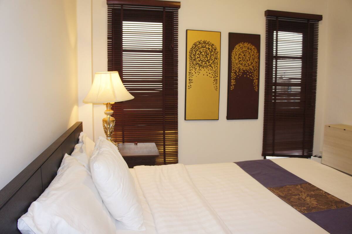 A hotel room with a bed, a nightstand, a lamp, and two wall art pieces.