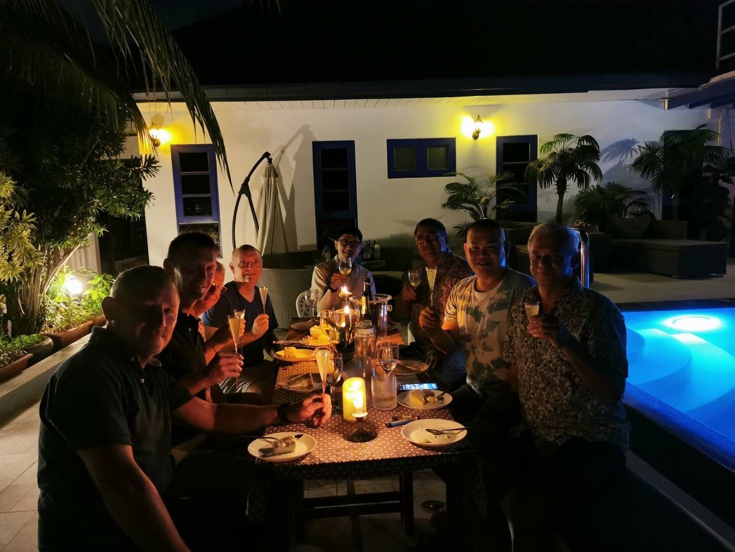A group of people dining outdoors at night with a pool in the background.