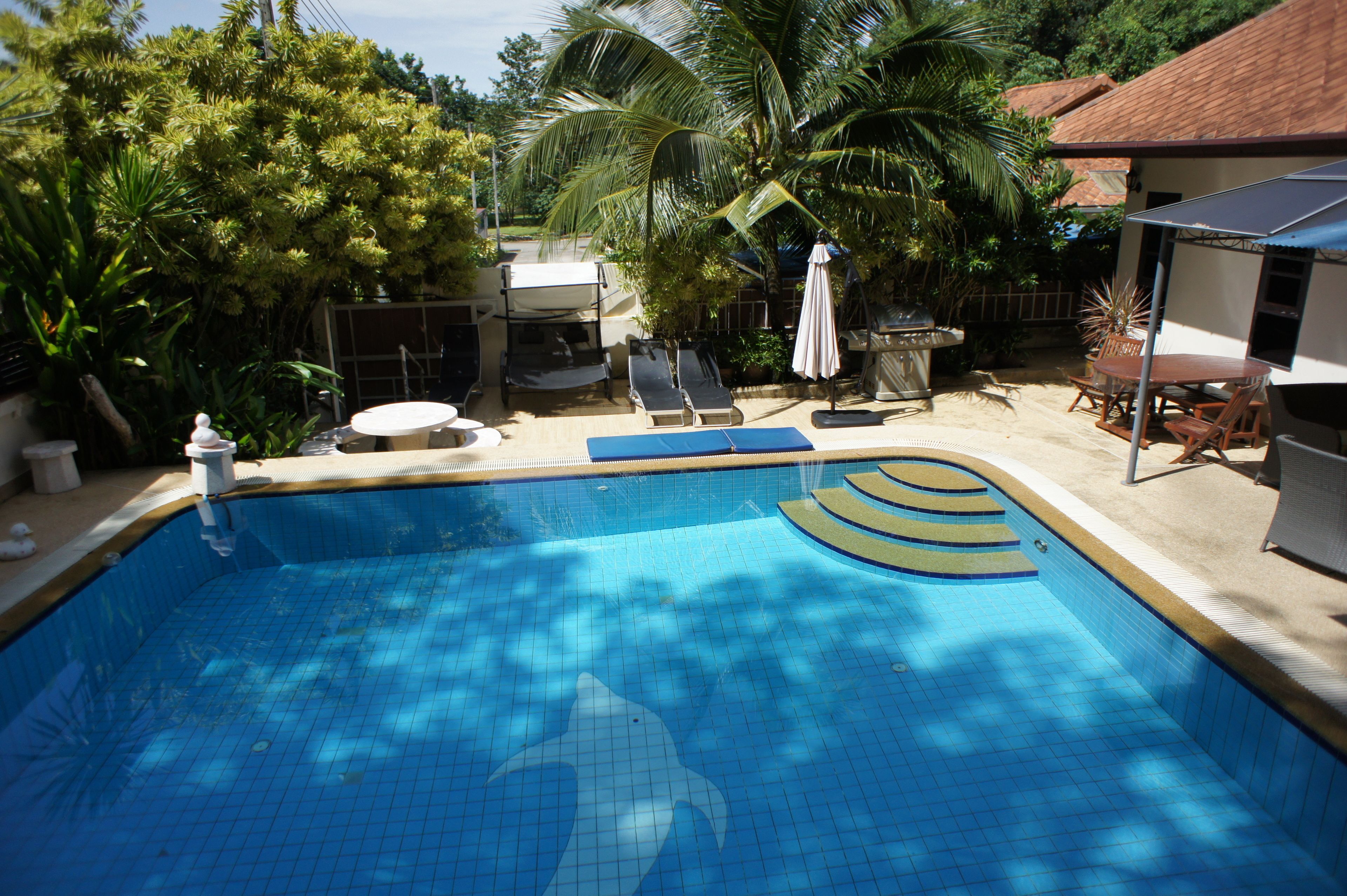 A swimming pool with a dolphin design, surrounded by palm trees and a covered patio area.