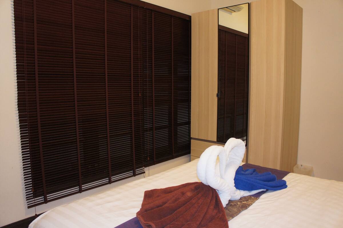 A hotel room with a bed, a brown towel, a blue towel, and a wooden wardrobe with a mirror.