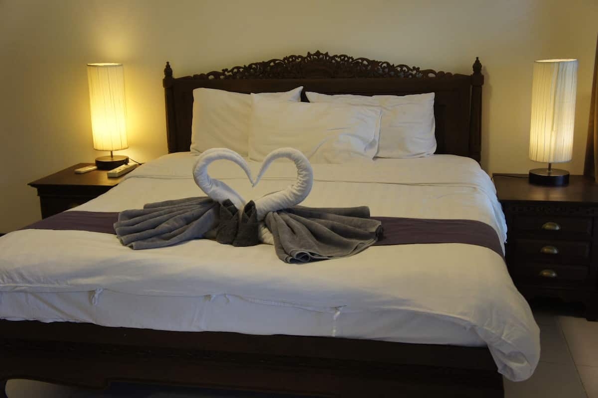A neatly made bed with a heart-shaped towel arrangement, a wooden headboard, and bedside lamps.