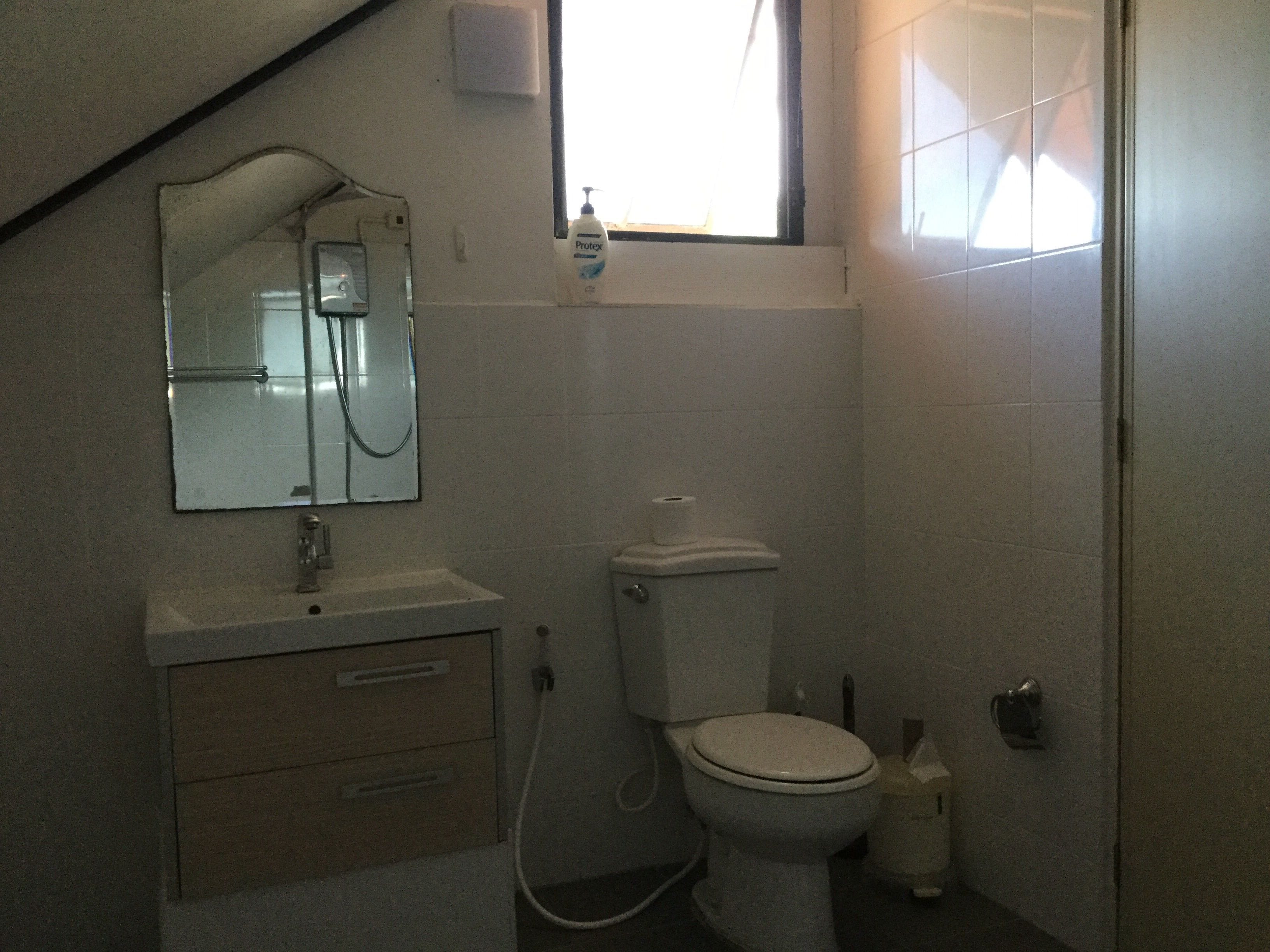 Een kleine, eenvoudige badkamer met toilet, wastafel en spiegel.