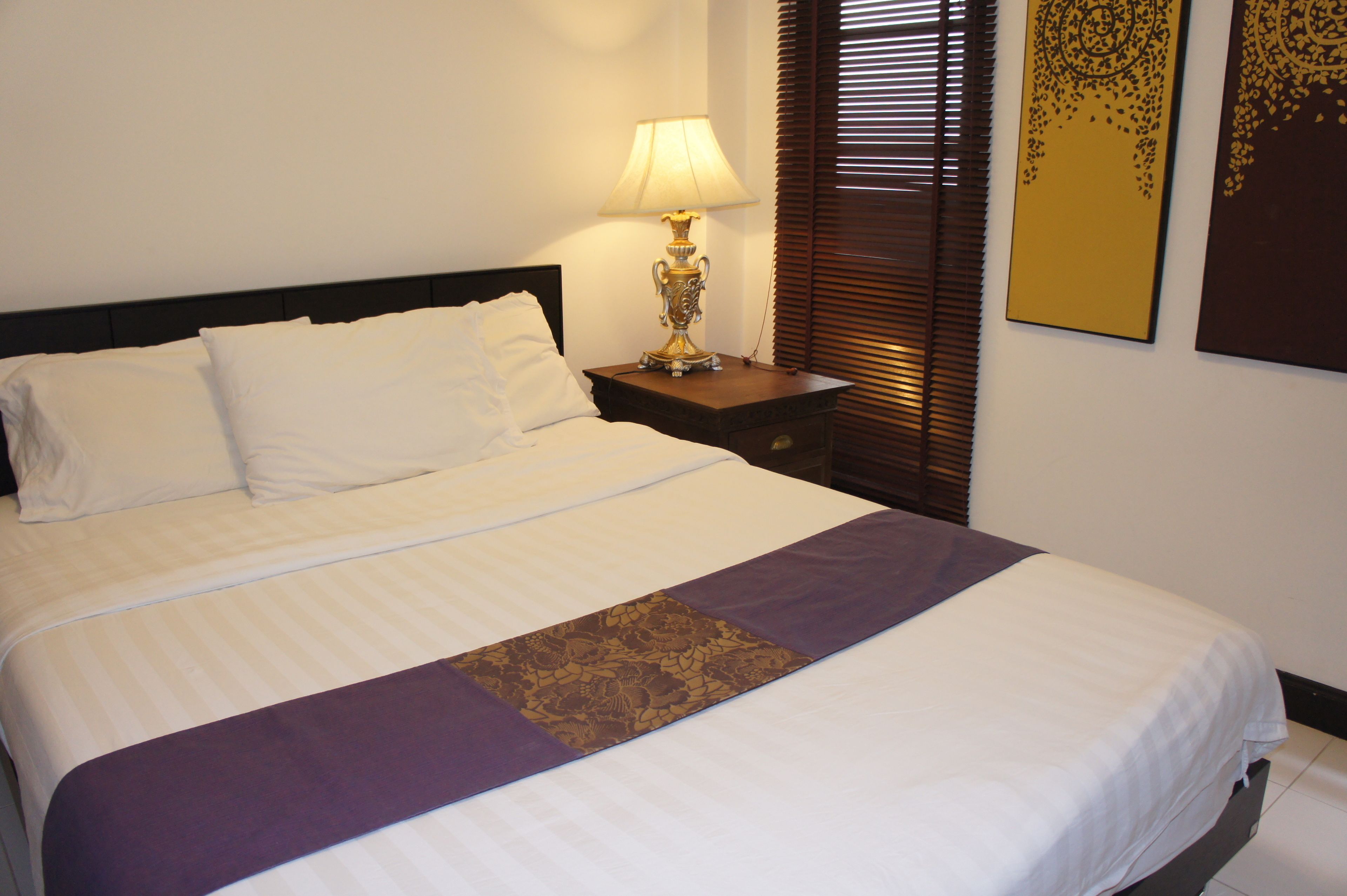 A neatly made bed with white linens and a purple accent runner.