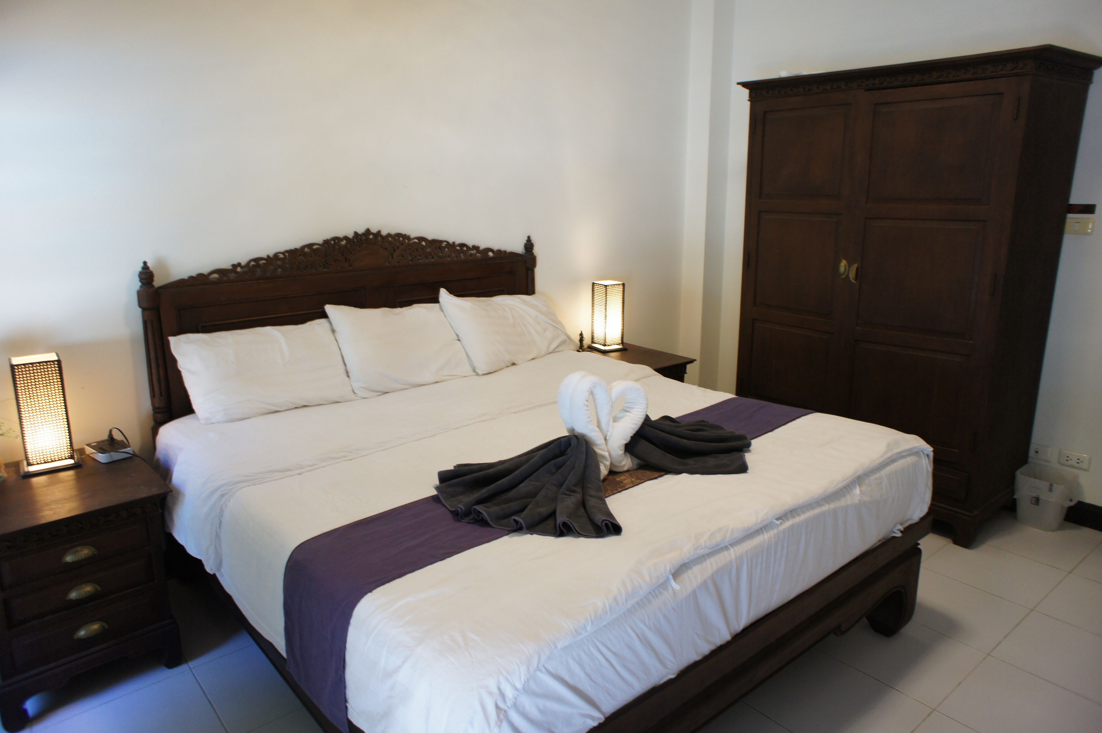 A neatly made bed with a towel and robes, a wooden wardrobe, and bedside lamps.