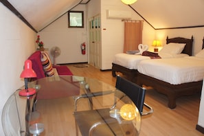 A hotel room with a glass dining table, two beds, a wooden floor, a fan, and a fire extinguisher.