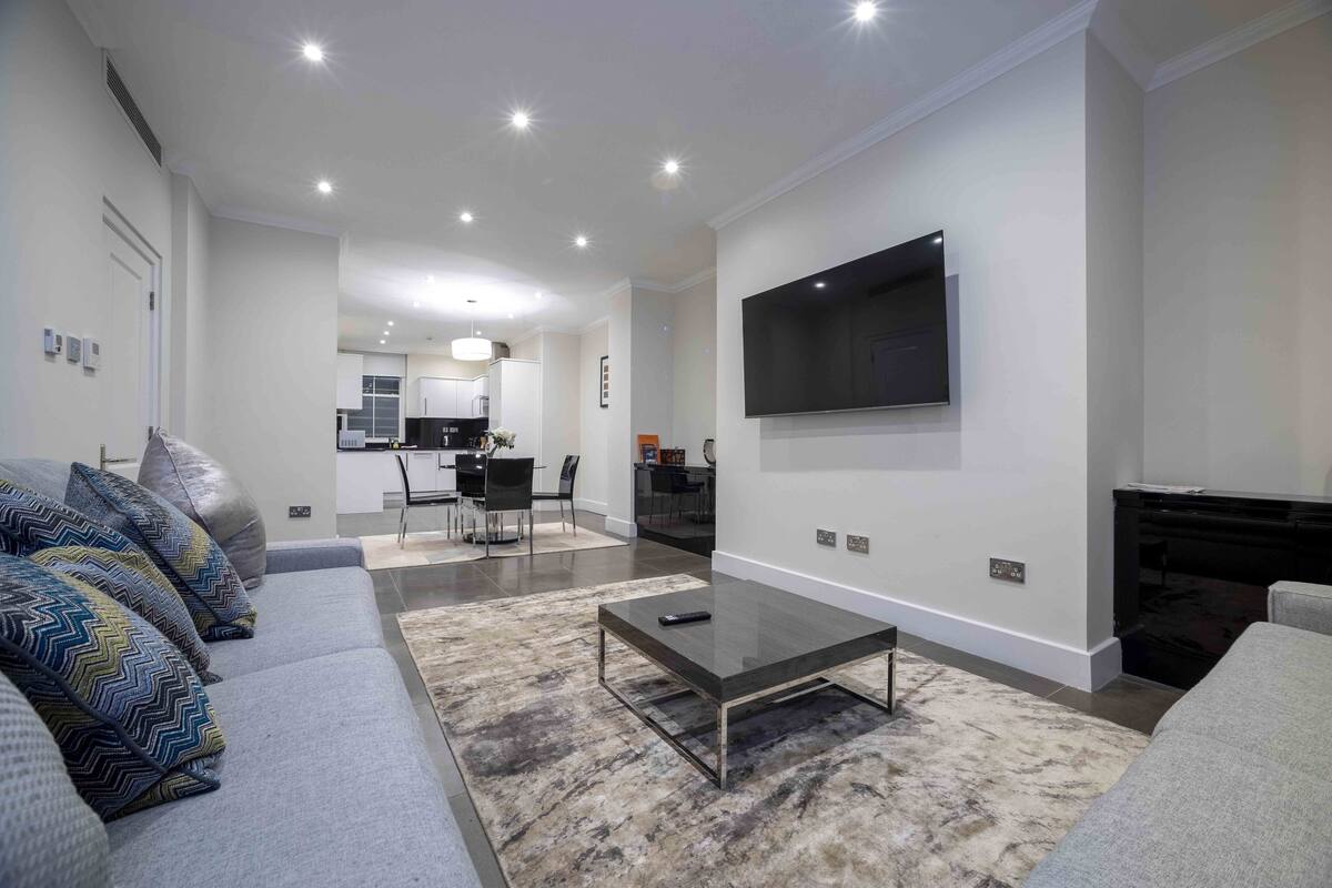 A modern living room with a grey sofa, a coffee table, and a flat-screen TV mounted on the wall.