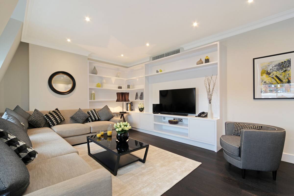 A modern living room with a sectional sofa, a black coffee table, a grey armchair, a flat-screen TV, and a white entertainment unit.