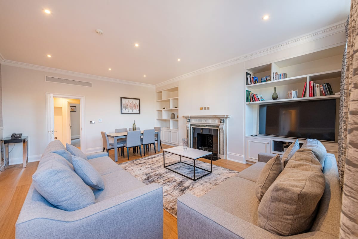 A modern living room with a sofa, coffee table, fireplace, television, and bookshelves.