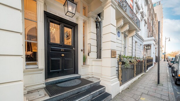 Une porte double noire portant le numéro 20, un escalier menant à l’entrée et une rampe en métal noir.