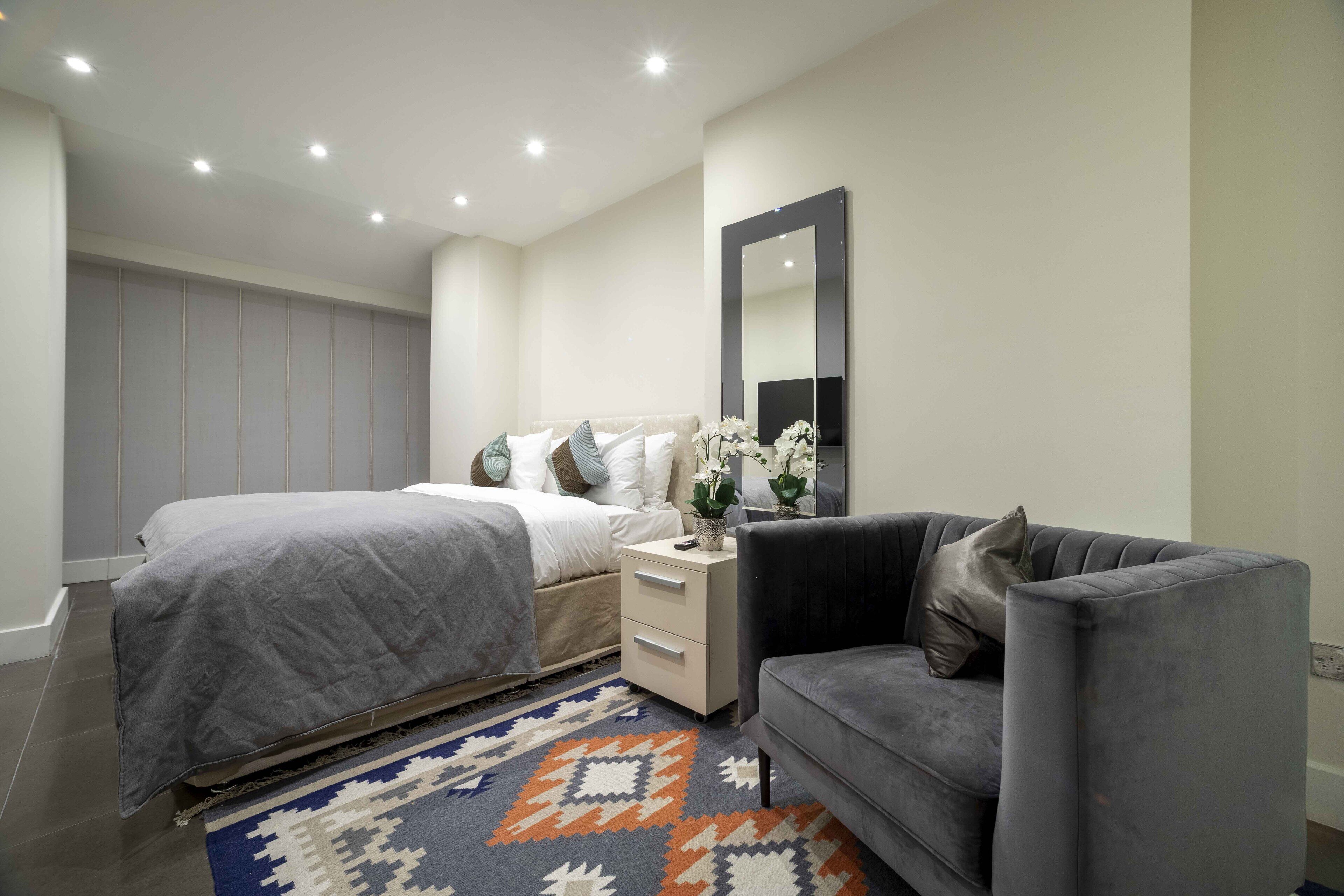 A modern bedroom with a bed, bedside table, and a grey sofa.