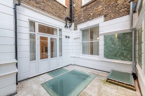 A narrow courtyard with white walls, a brick upper section, and a green-tiled floor. - 20 Hertford Street (London)
