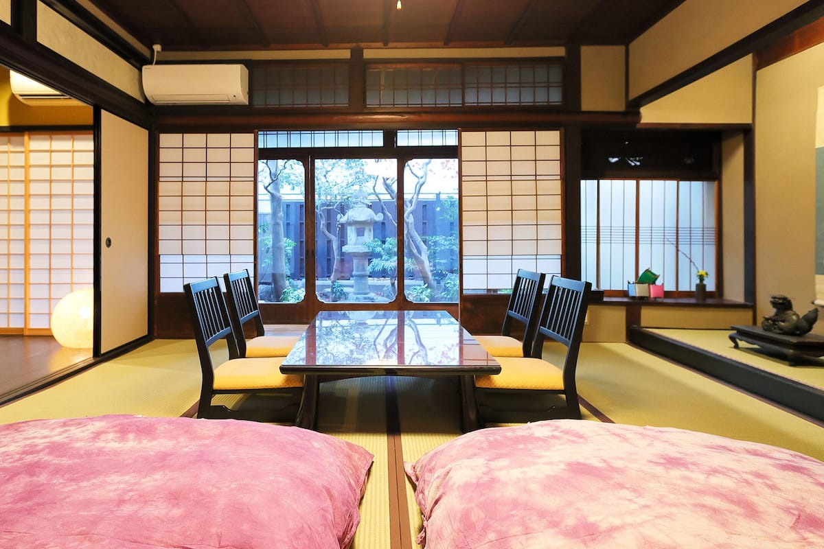 Una habitación japonesa tradicional con suelo de tatami, una mesa baja con cojines y puertas correderas.