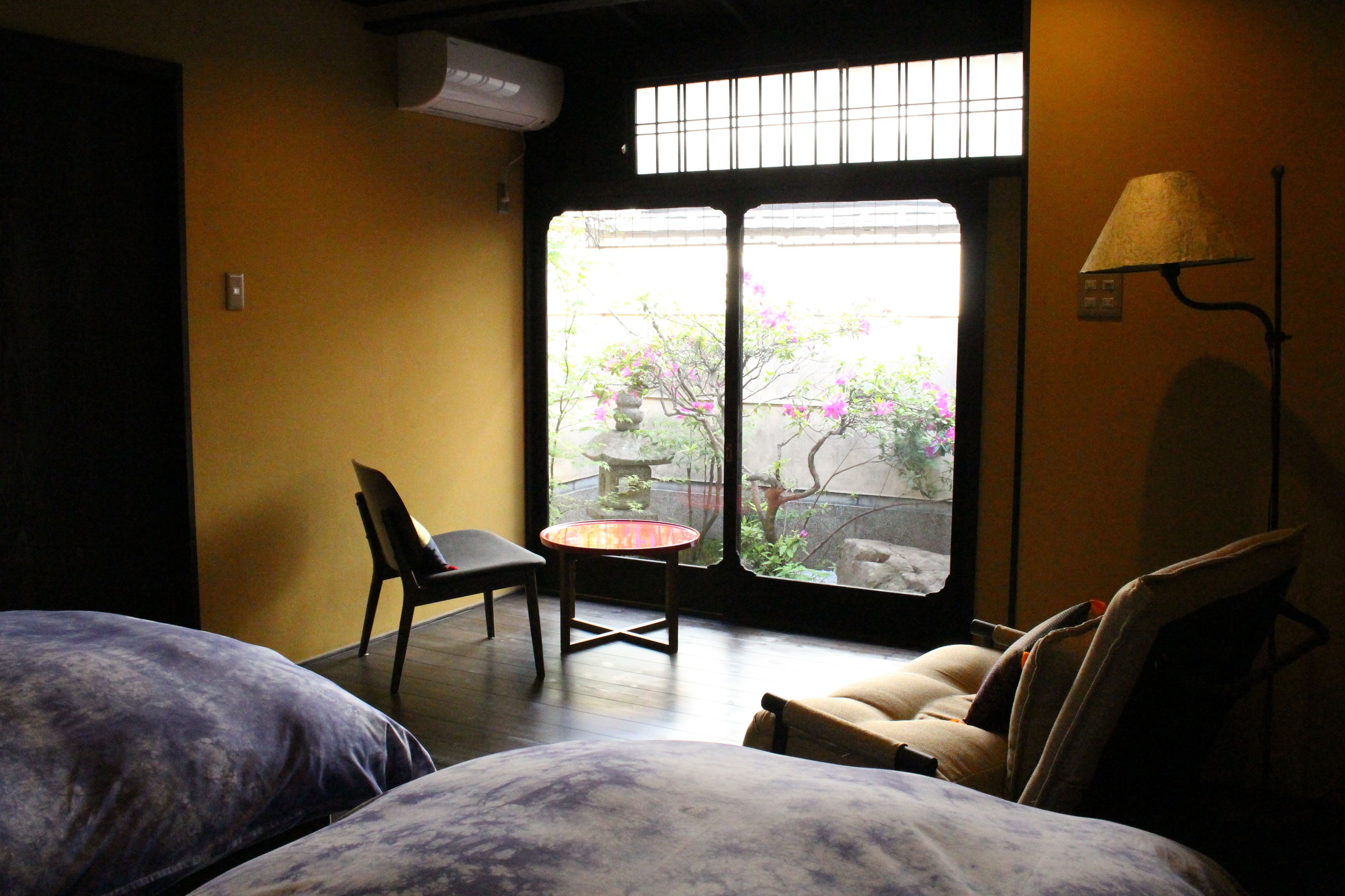 Habitación de hotel con cama, una silla, una mesita y ventana con vistas a un jardín.