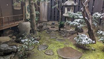 Un jardín con faroles de piedra, suelo cubierto de musgo y árboles.