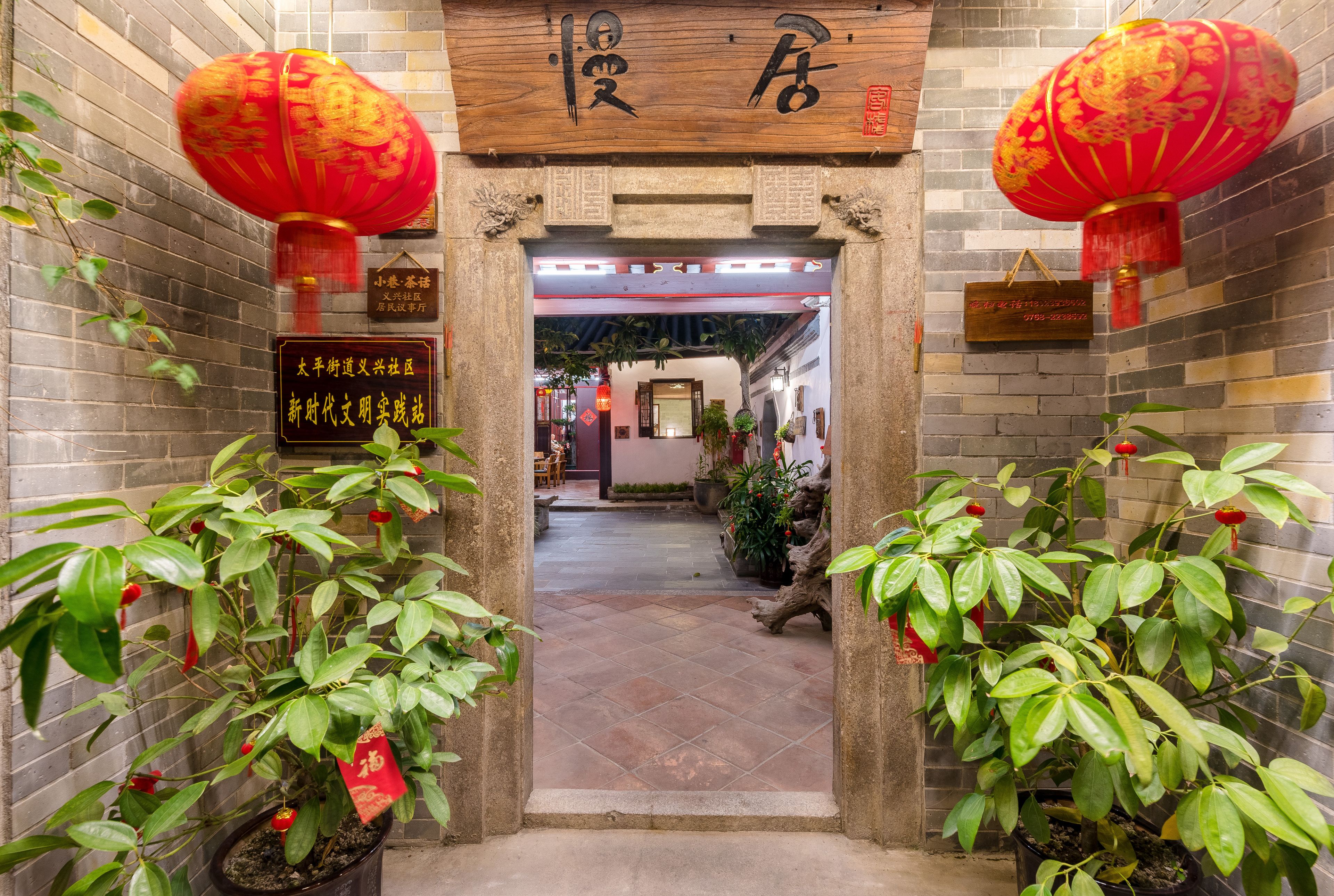 A traditional Chinese entrance with red lanterns, potted plants, and a signboard.