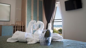 Habitación de hotel con cama, televisor montado en la pared, ventana con vista a la playa y un minibar.