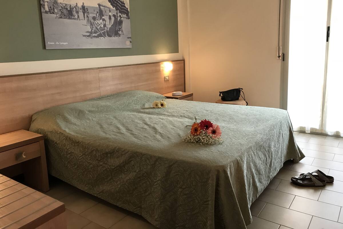Hotelkamer met een bed, nachtkastje, lamp, klein tafeltje en een foto aan de muur.