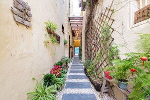 Une ruelle étroite avec un chemin pavé de pierres, des plantes en pot et des structures en treillis de bois.