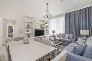 A modern living room with a dining table, sofas, a TV, and built-in shelves. - Chesham Court (London)