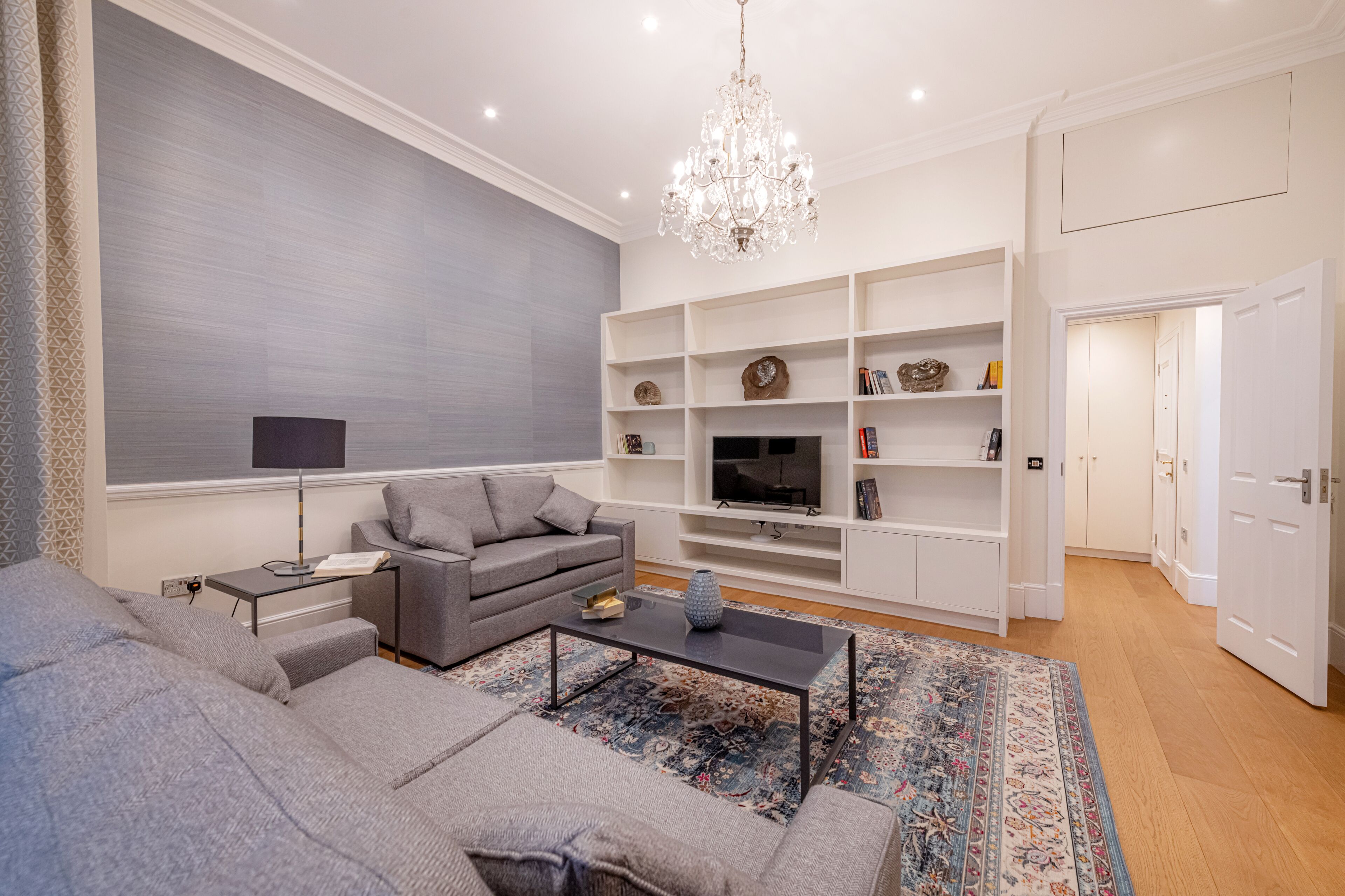 Ein modernes Wohnzimmer mit einem grauen Sofa, einem Couchtisch, einem Fernseher und einer Chandelüster.