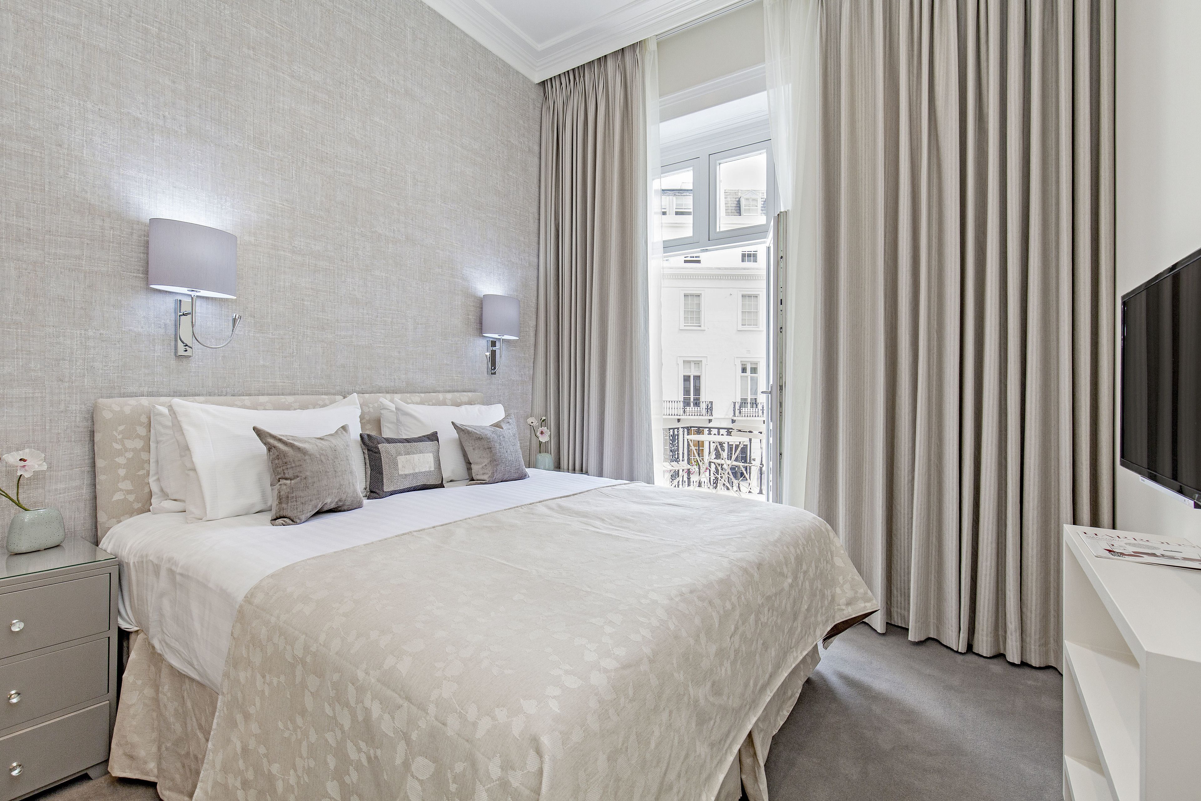 Une chambre d’hôtel moderne, dotée d’un grand lit, d’un bureau et offrant une vue sur la ville à travers de fines rideaux.