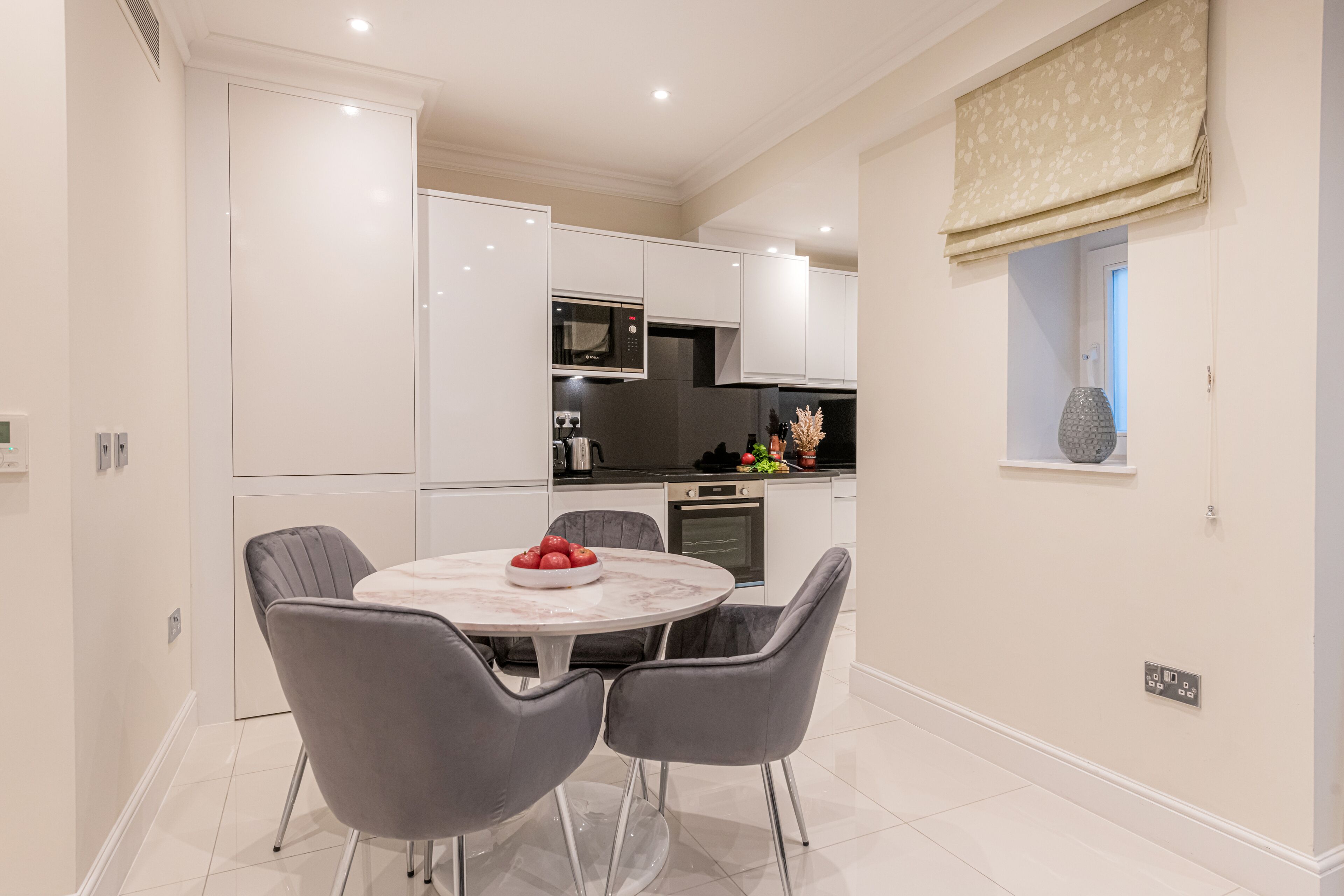 A modern kitchen with white cabinets, a marble countertop, and a dining table with two chairs.