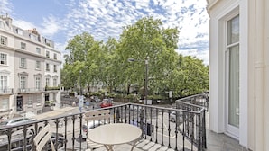 Un balcon avec une table et des chaises, donnant sur une rue animée où l’on peut voir des voitures et des immeubles.
