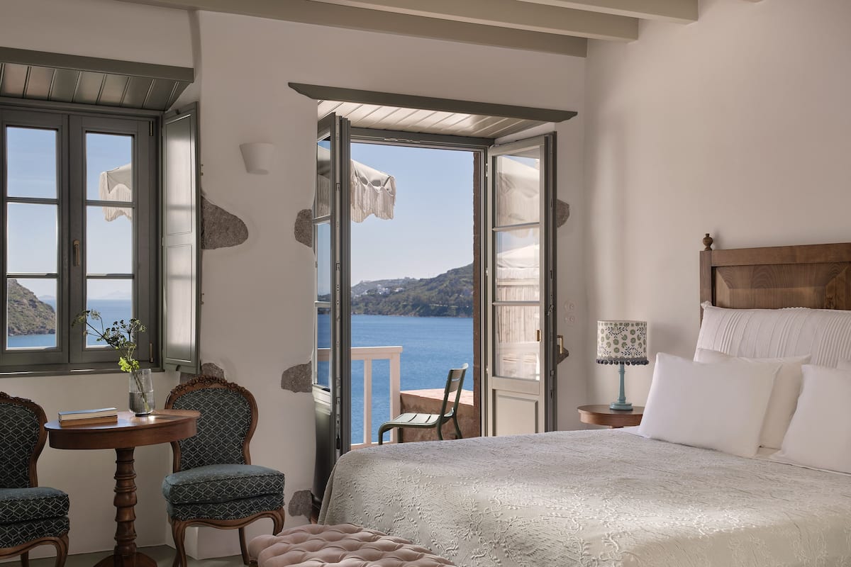 A bedroom with a bed, a chair, a table, and a view of the sea.