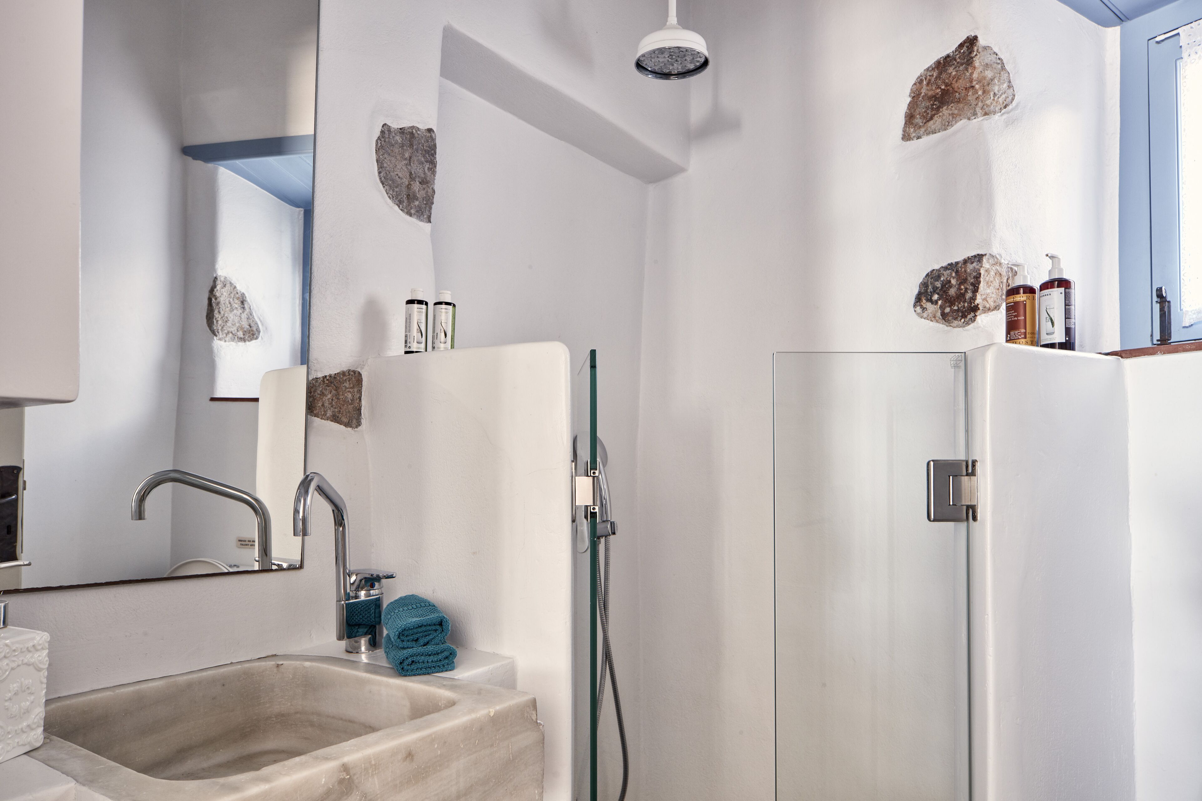 Un baño con lavamanos, espejo, ducha y artículos de aseo en la encimera.