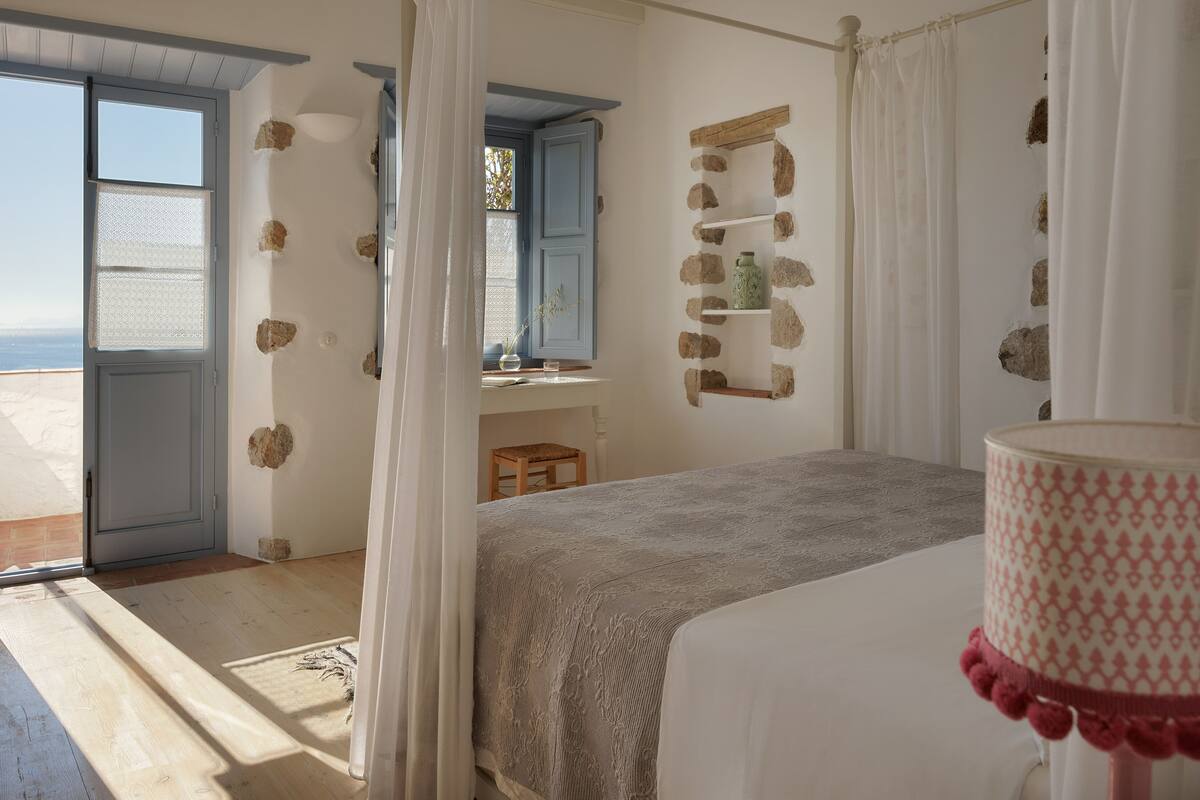 A bedroom with a bed, a window, a door, and a stone wall.