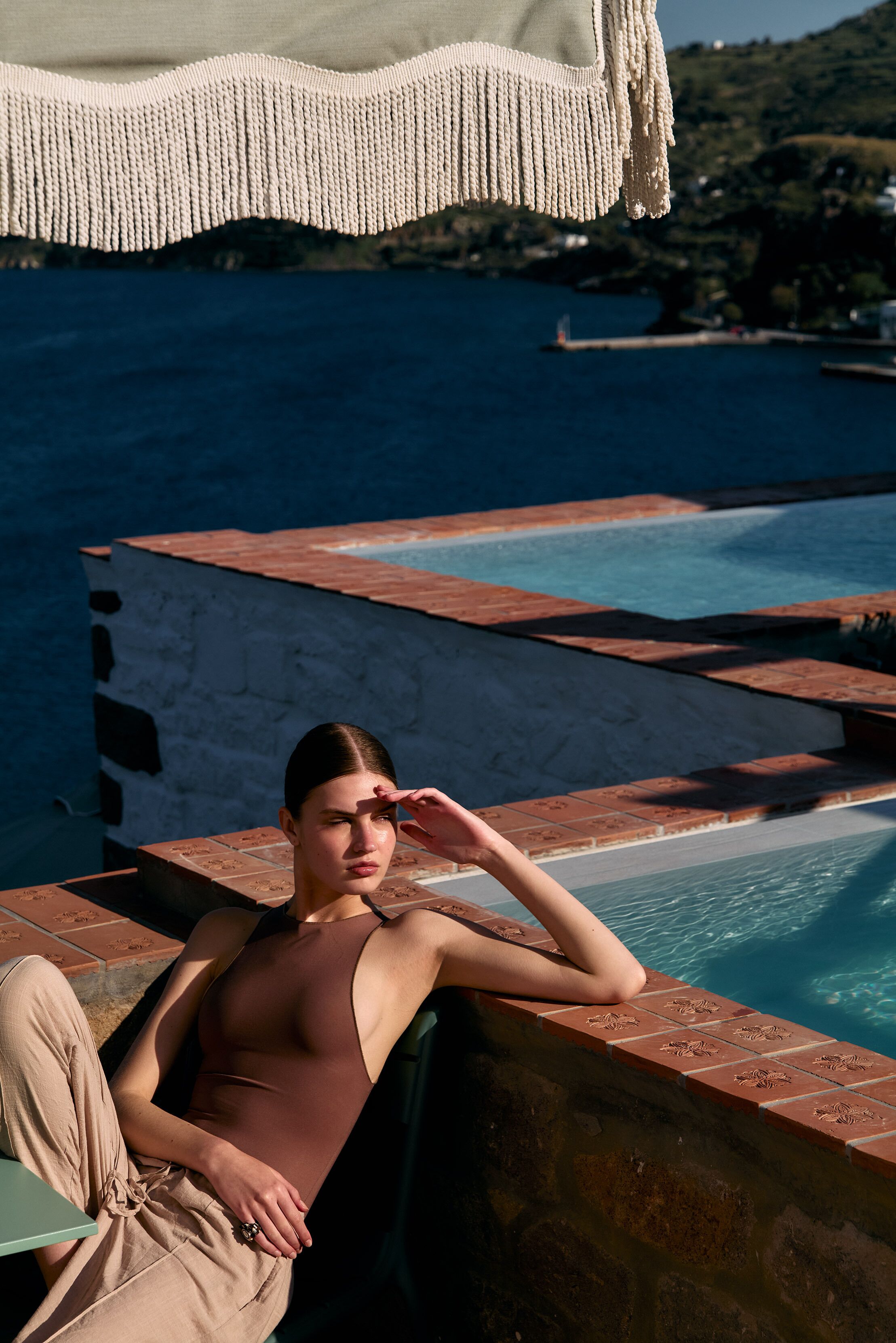 Una persona relajándose junto a una piscina con vistas al mar y un paisaje montañoso.