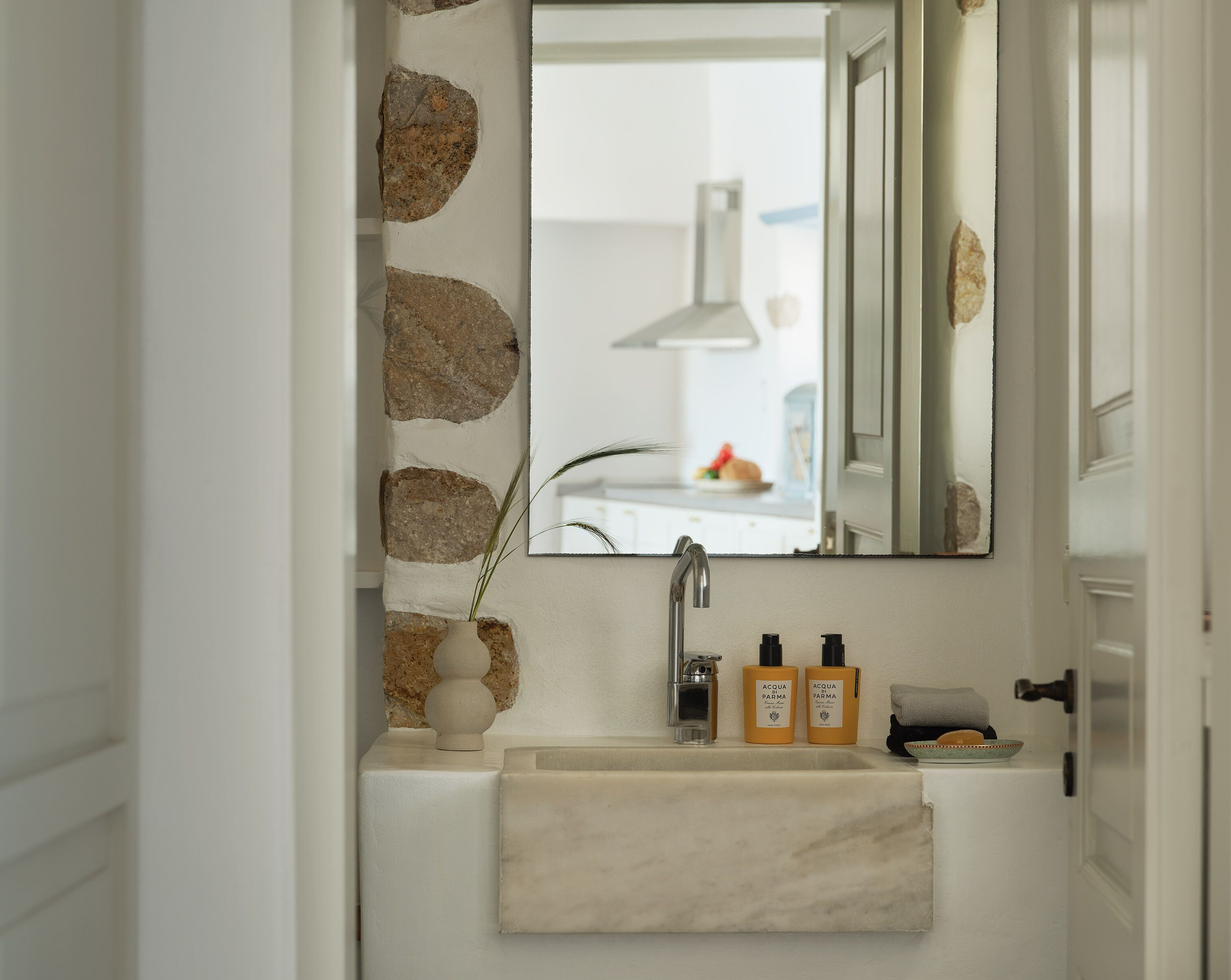 Un baño con lavamanos de mármol, dos botellas de Acqua Parma, una toalla y un espejo que refleja una zona de cocina.