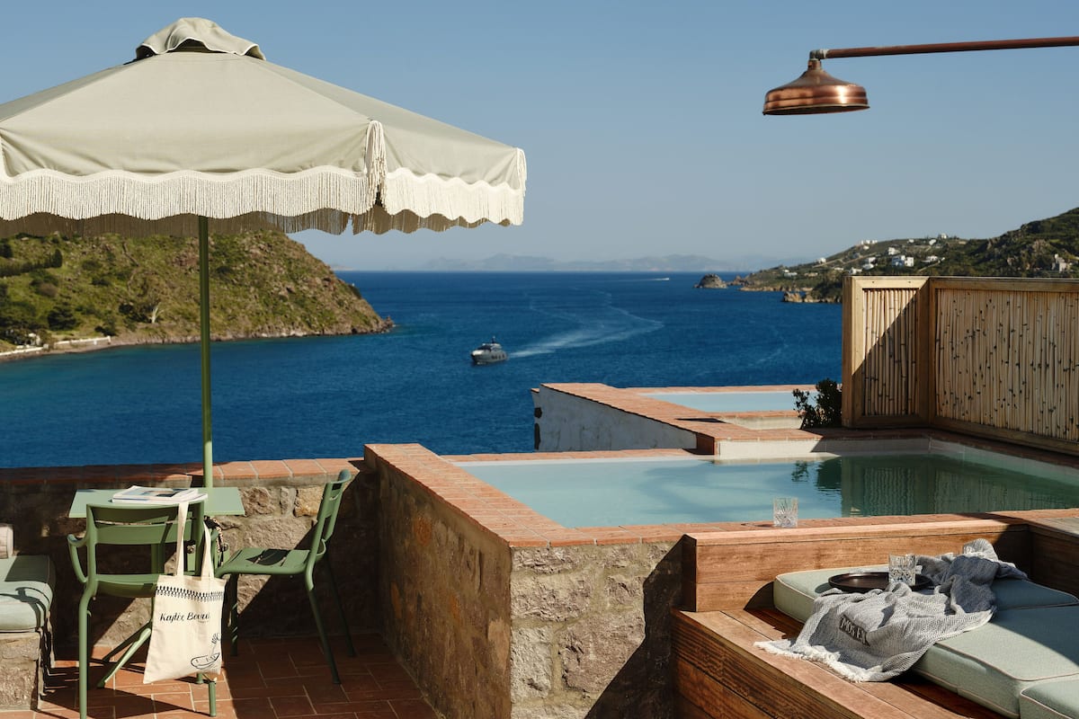 A poolside area with a view of the sea, a table with chairs, and a wooden deck.