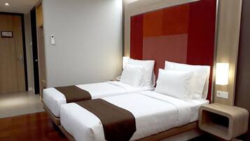 Een hotelkamer met twee bedden, een houten vloer, een rode accentmuur en een nachtkastje met een lamp.
