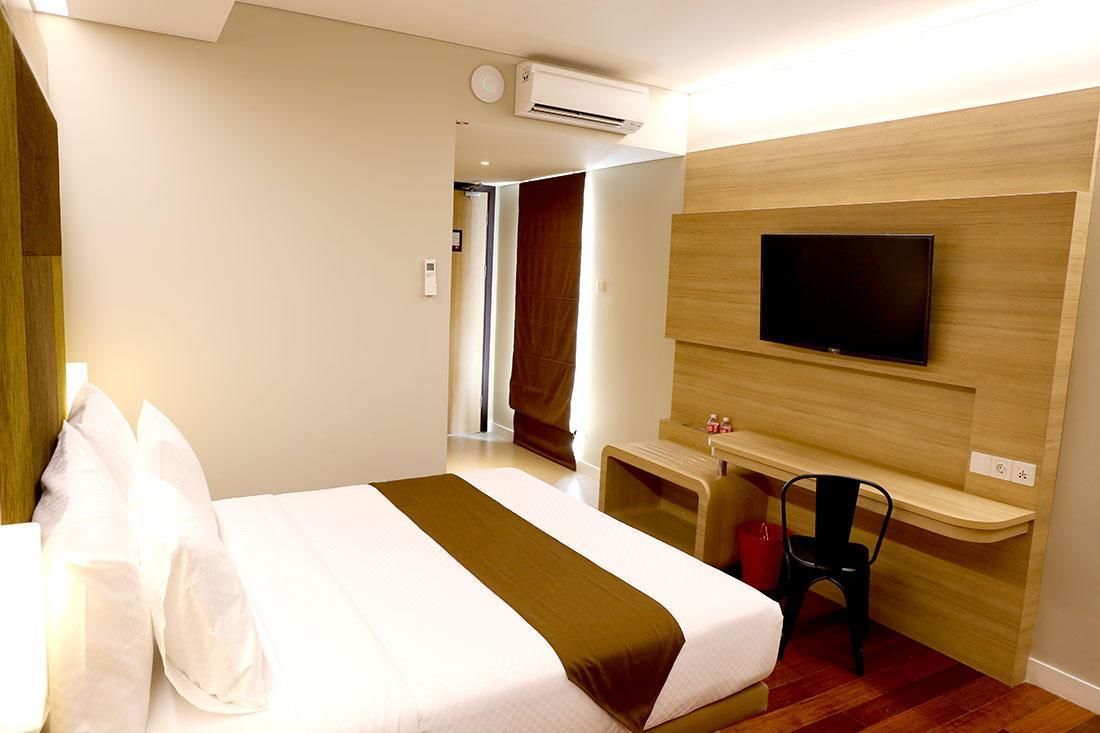 A hotel room with a bed, a TV mounted on the wall, a desk, and a chair.