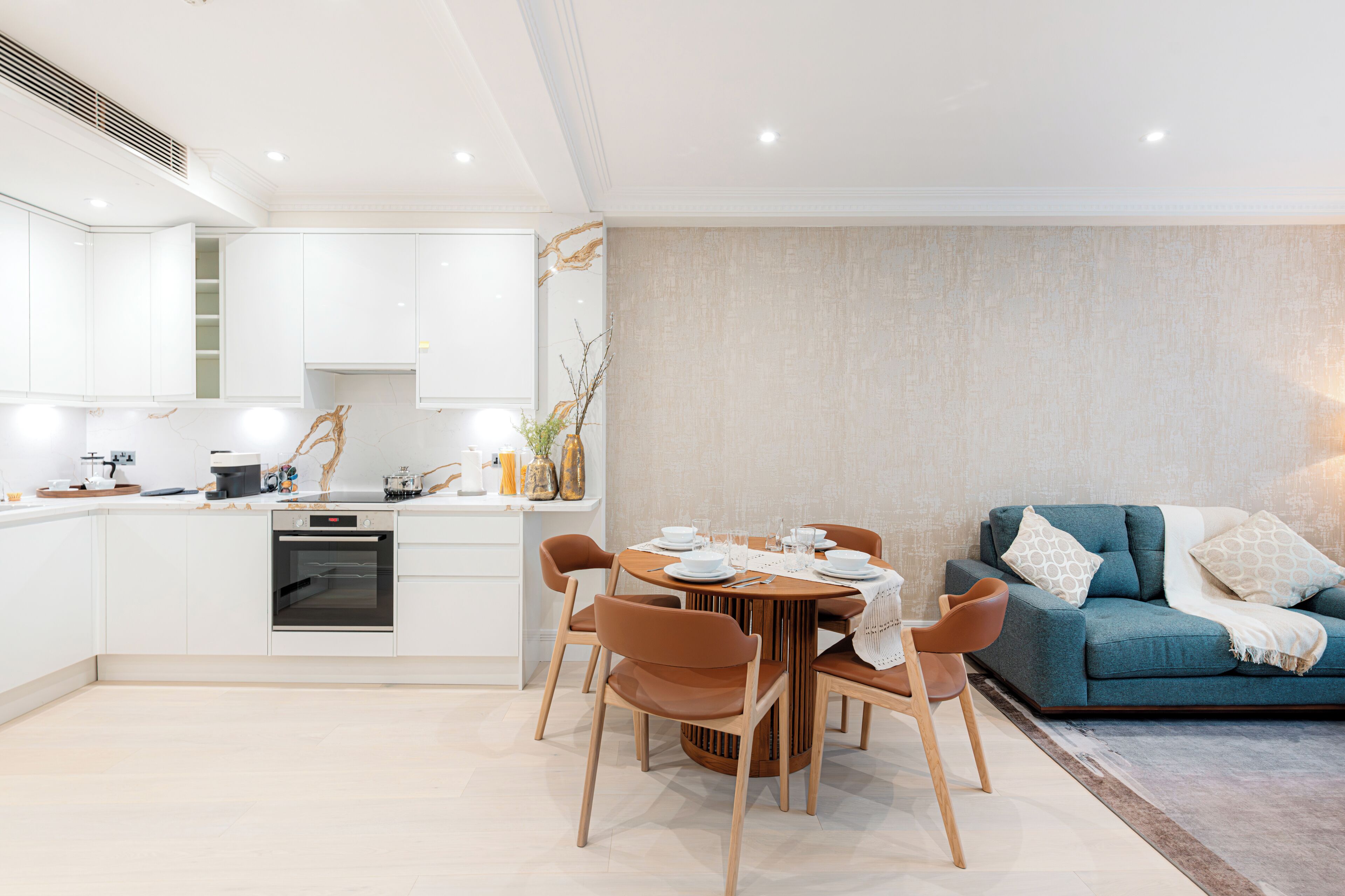 Una cocina moderna con armarios blancos, horno empotrado y comedor con mesa redonda y sillas.