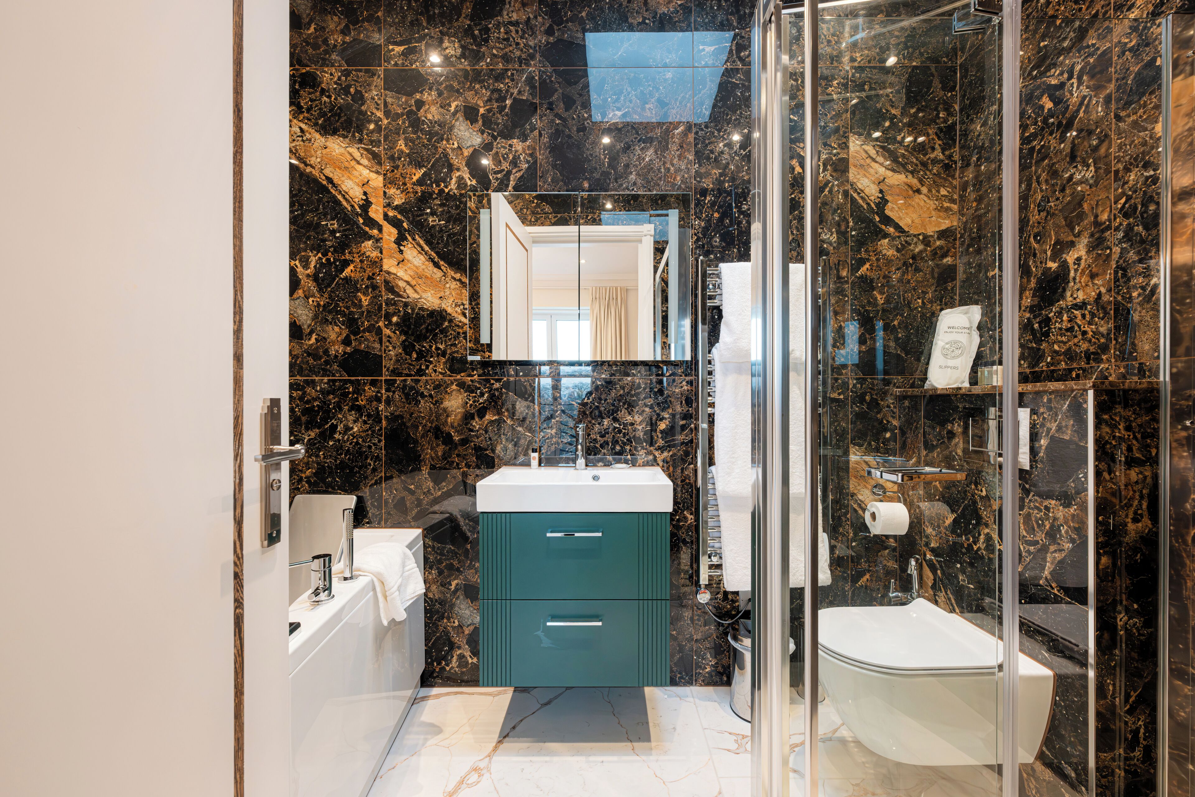 A modern bathroom with a marble backsplash, a glass shower enclosure, and a white sink.