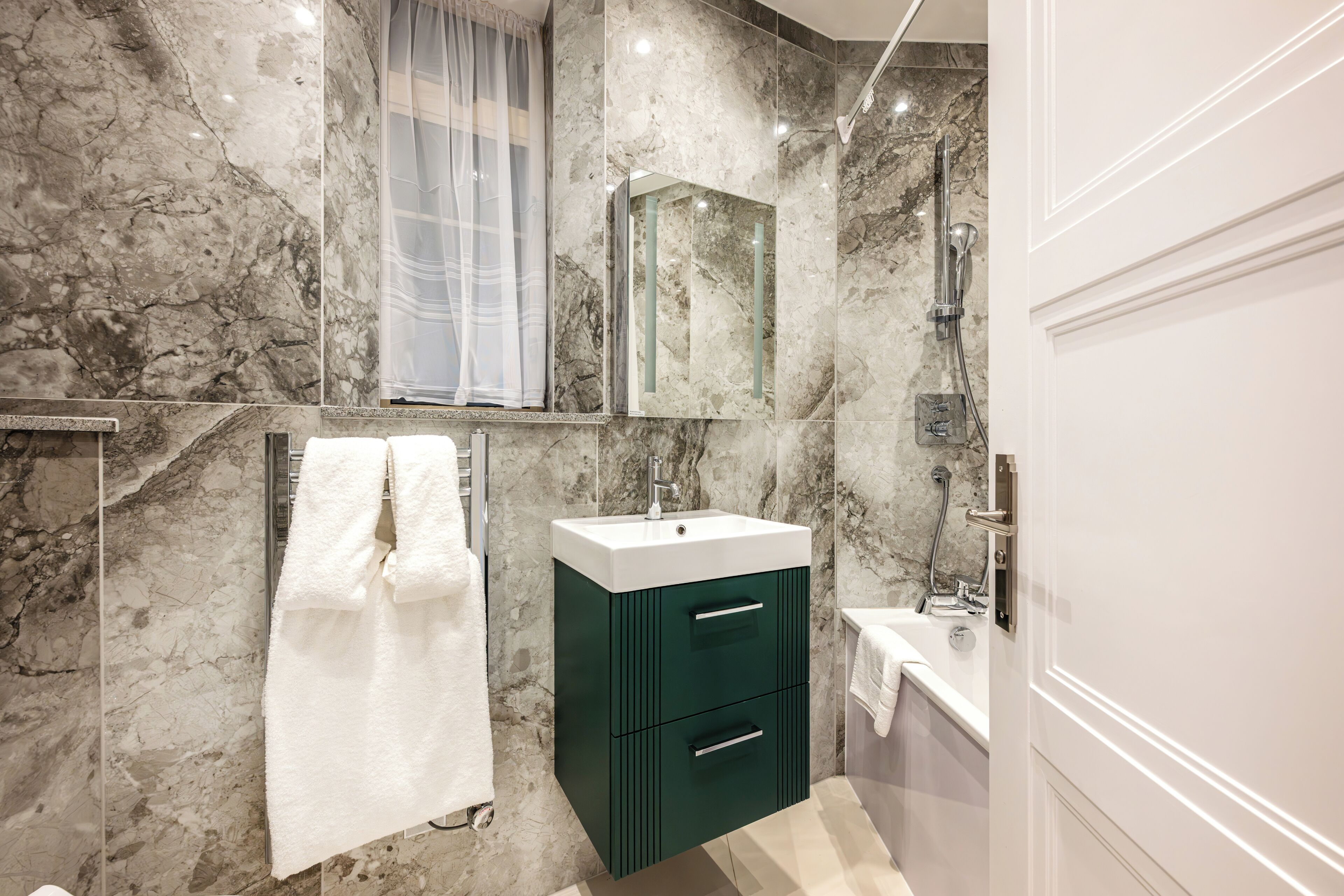 A modern bathroom with a marble wall, a white sink, a green cabinet, and a bathtub.